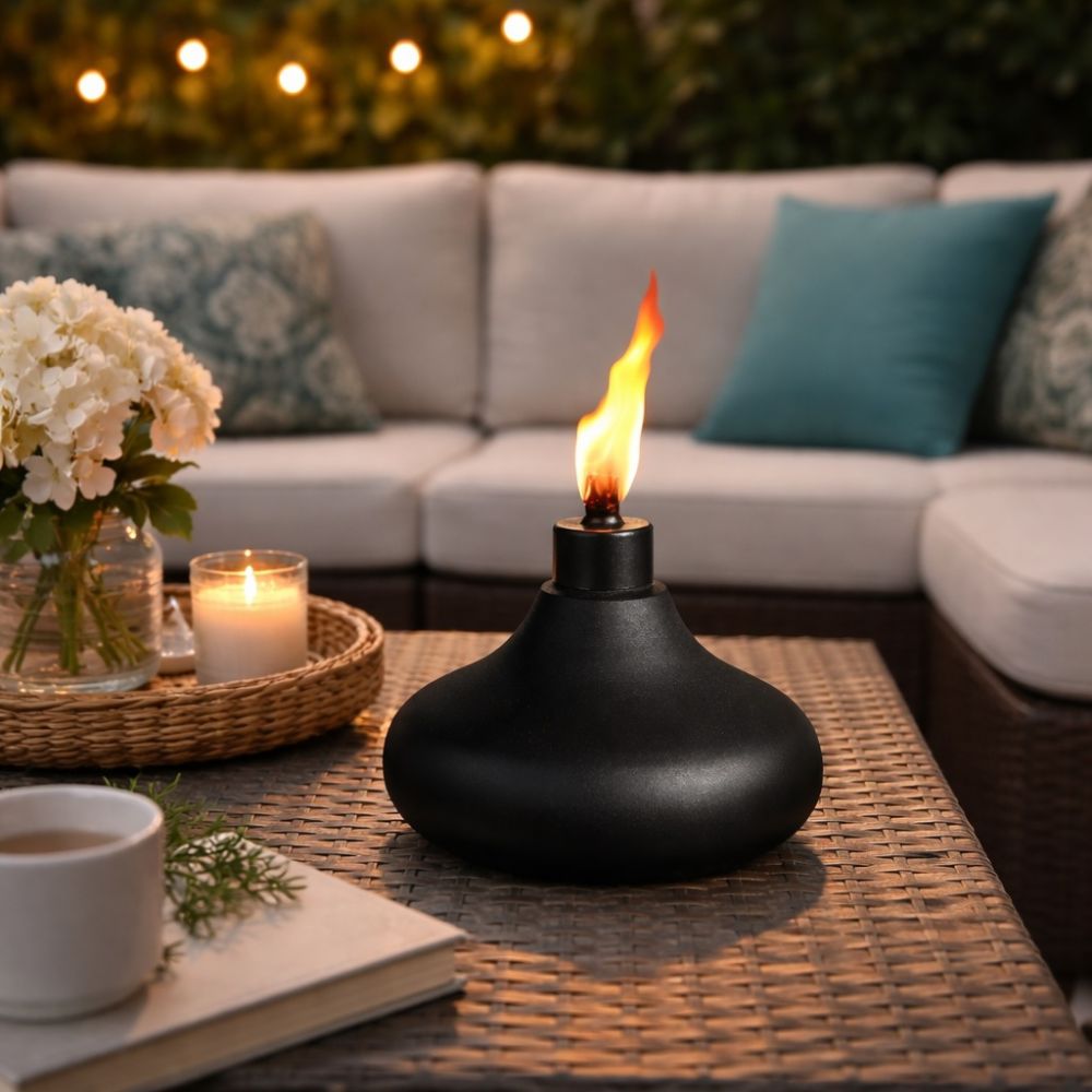 Lampe noire avec une flamme posée sur une table basse de jardin, avec un canapé en arrière-plan