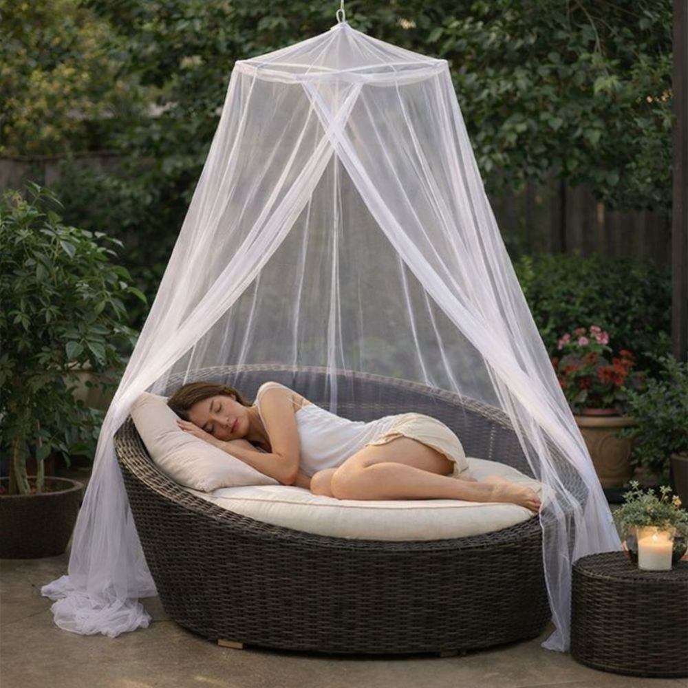 Femme qui dort dans un fauteuil de forme ronde dans un jardin, avec au-dessus d'elle une moustiquaire baldaquin blanche